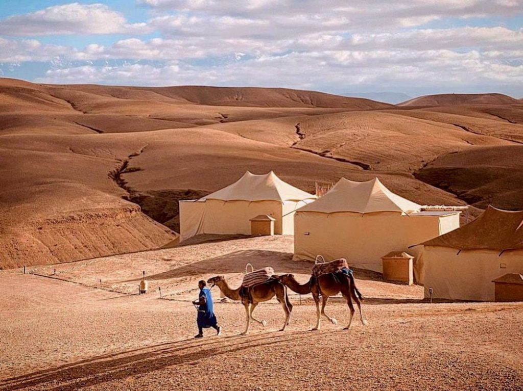 Luxury desert camp in Agafay with stylish tents, glowing lanterns, and views of the Atlas Mountains at night.
