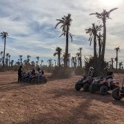 Un rider en quad sur une piste poussiéreuse avec les montagnes de l'Atlas en arrière-plan.