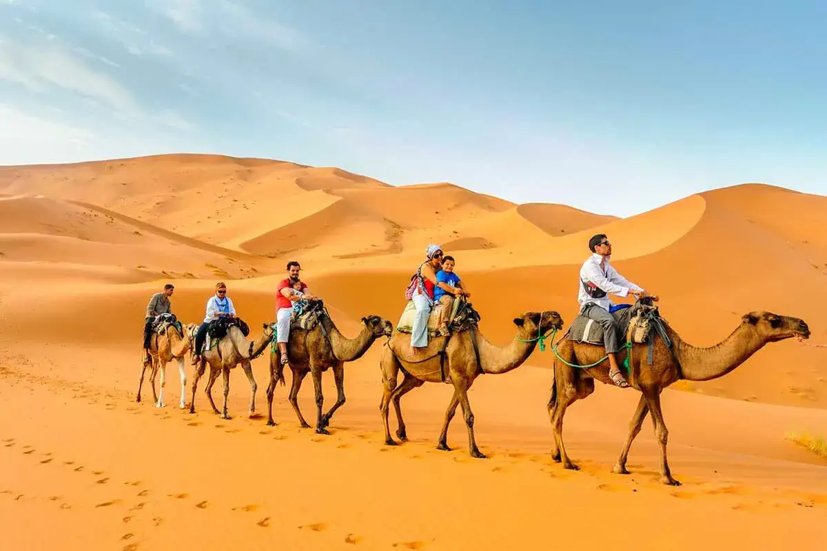 Cavaleiros de camelo a atravessar dunas cor de laranja – Viagem de 4 Dias ao Deserto a Partir de Marrakech